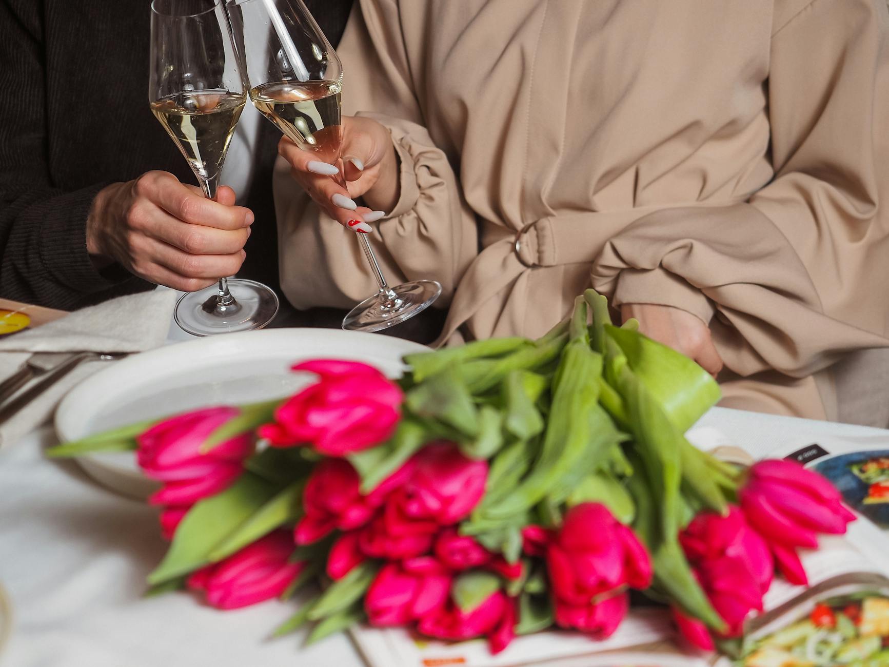 tulips on table and couple hands holding glasses of champagne. Photo by Nadin Sh on Pexels.com