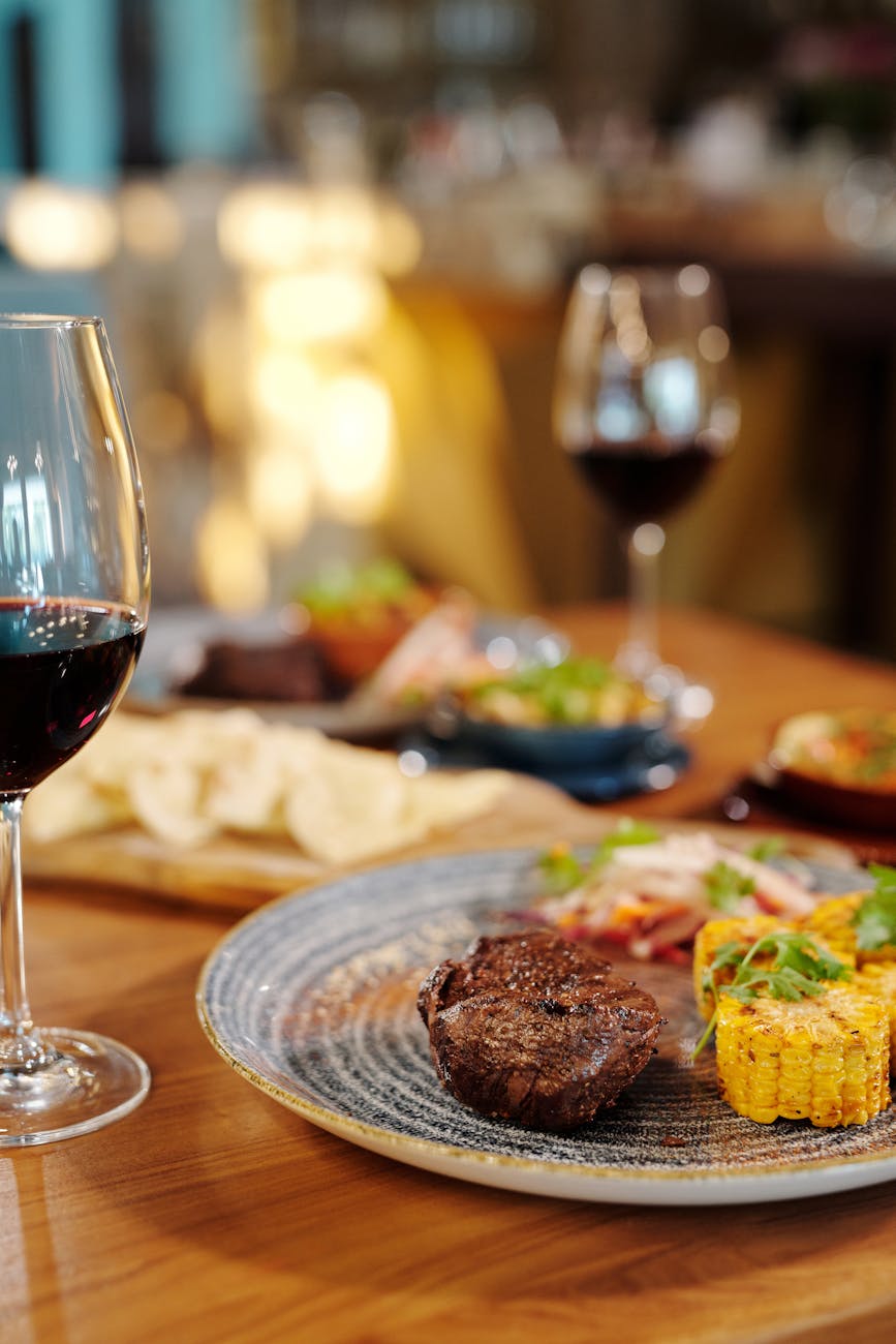 cooked food on ceramic platebeside a glass of red wine. Photo by Jep Gambardella on Pexels.com